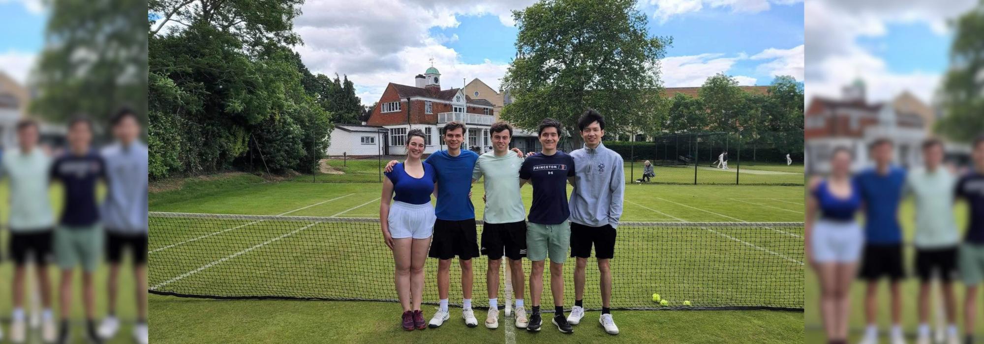 one young woman and four young men on a lawn tennis court, standing for a photo at the net