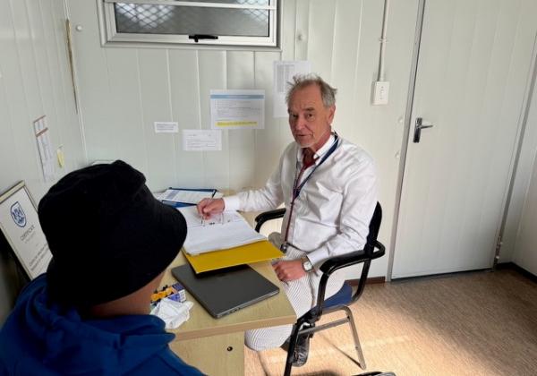 Professor Wilkinson OBE seated in the clinic with a patient seated with his back to the camera