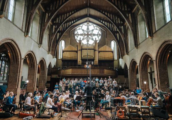 Choir and full orchestra surrounded by microphones and lit by a large church window
